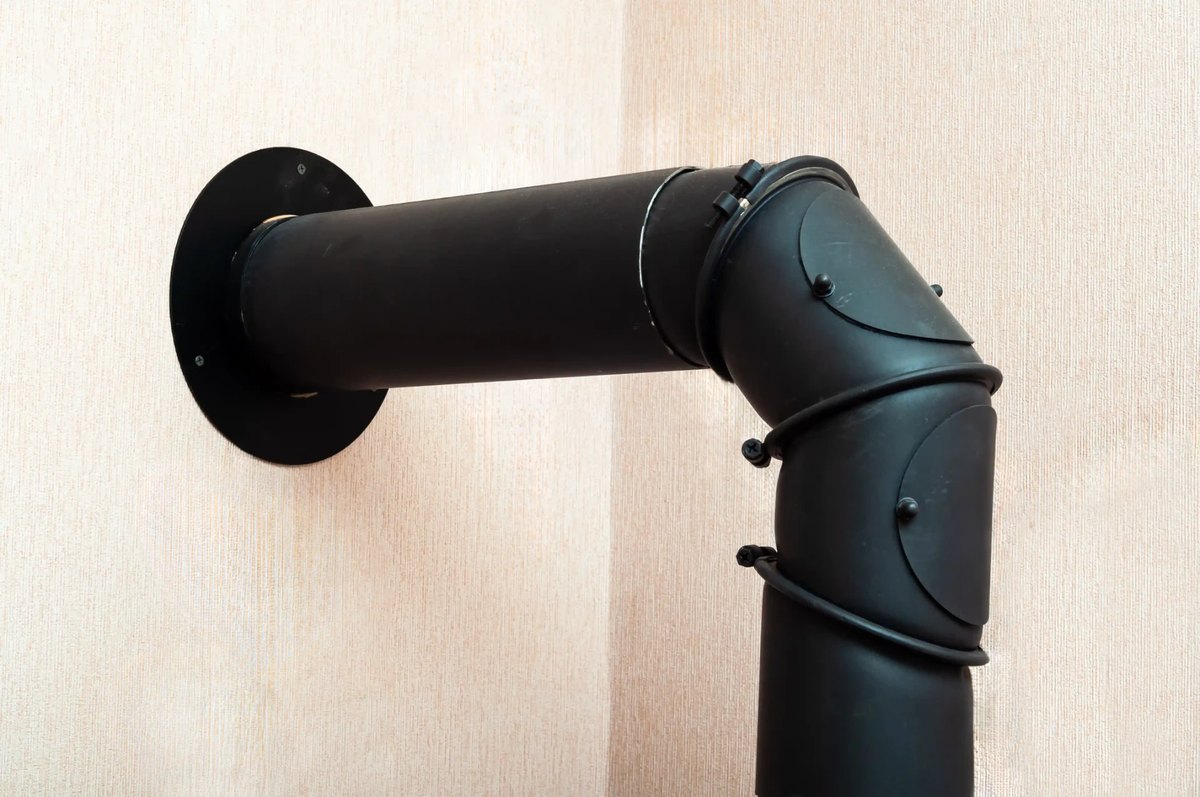 Close-up of a black flue pipe venting through a wall with a safe clearance