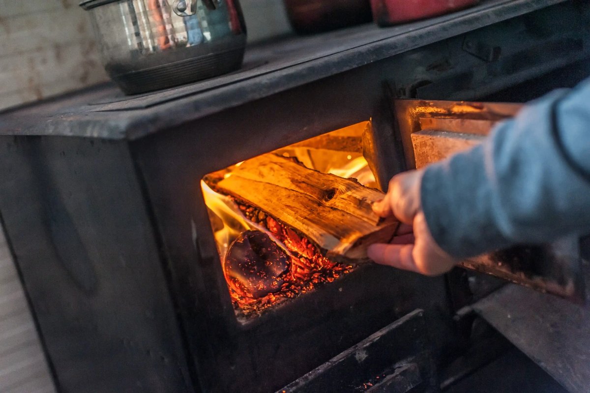 Person loading firewood into a wood stove following safe operating practice
